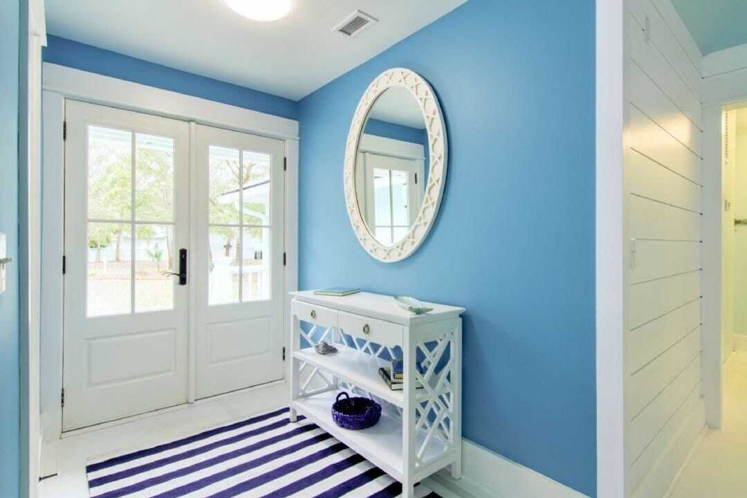 Un couloir avec une console blanche, un mur bleu et une porte blanche dotée de panneaux de verre.