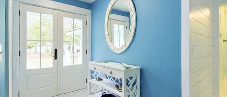 Un couloir avec une console blanche, un mur bleu et une porte blanche dotée de panneaux de verre.