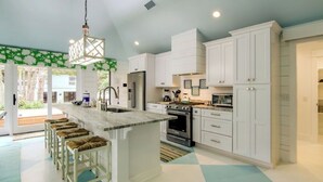 A kitchen with white cabinets, a central island with stools, a refrigerator, an oven, and a hanging light fixture. - 12 Abalone Alley by Avantstay Close to Beach w/ Pool & BBQ (Isle of Palms)