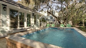 A swimming pool with a wooden deck, a covered patio, and a view of a house with large windows and a fence. - 12 Abalone Alley by Avantstay Close to Beach w/ Pool & BBQ (Isle of Palms)