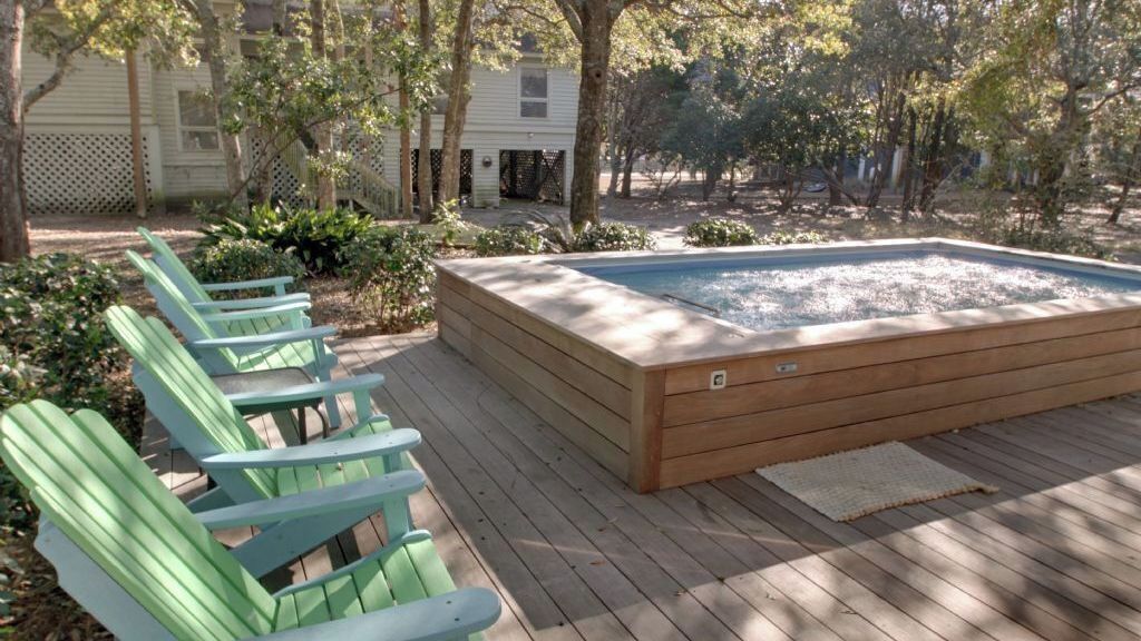 Une terrasse en bois avec un jacuzzi, des fauteuils Adirondack verts et une clôture en bois.