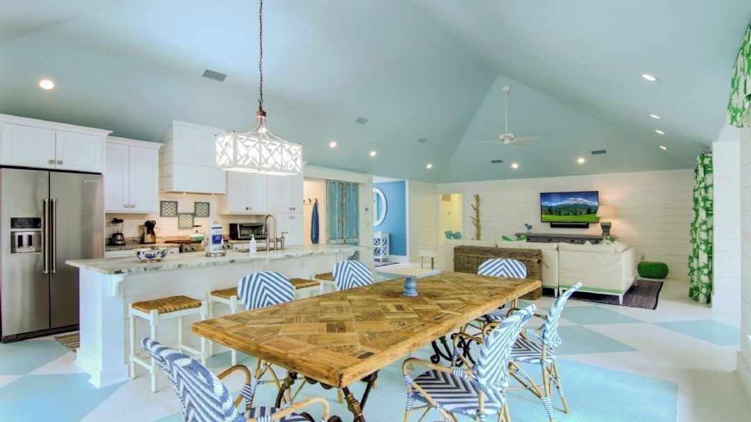 A modern kitchen with white cabinets, a large island, and a dining area with striped chairs.