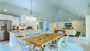 A modern kitchen with white cabinets, a large island, and a dining area with striped chairs. - 12 Abalone Alley by Avantstay Close to Beach w/ Pool & BBQ (Isle of Palms)
