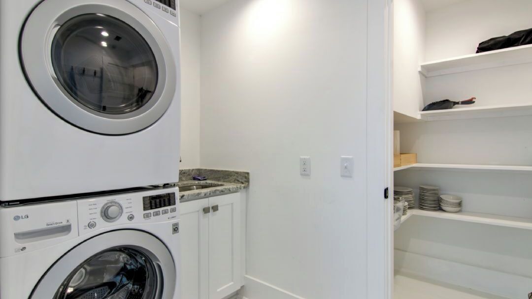 A laundry room with stacked washers and dryers, white walls, and shelves with folded clothes.