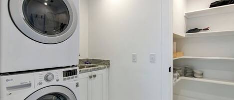 A laundry room with stacked washers and dryers, white walls, and shelves with folded clothes.