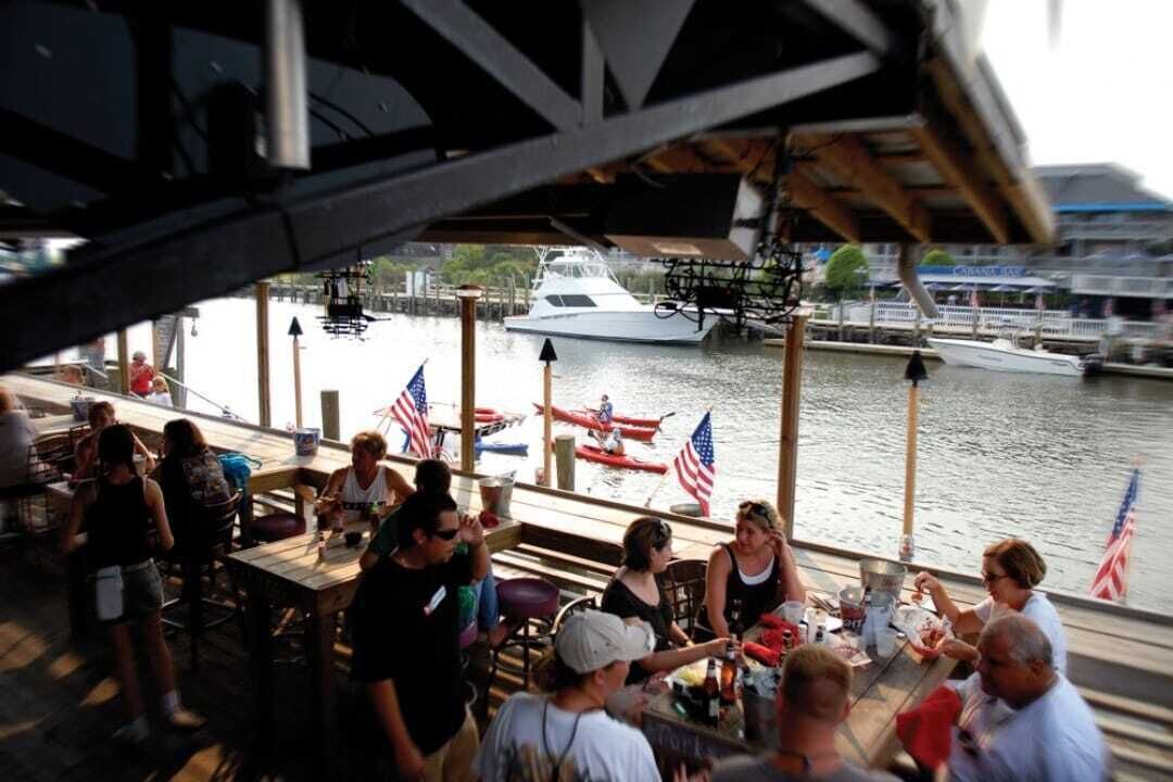 Une terrasse de restaurant avec des places assises extérieures, offrant une vue sur une marina avec des bateaux et un quai.
