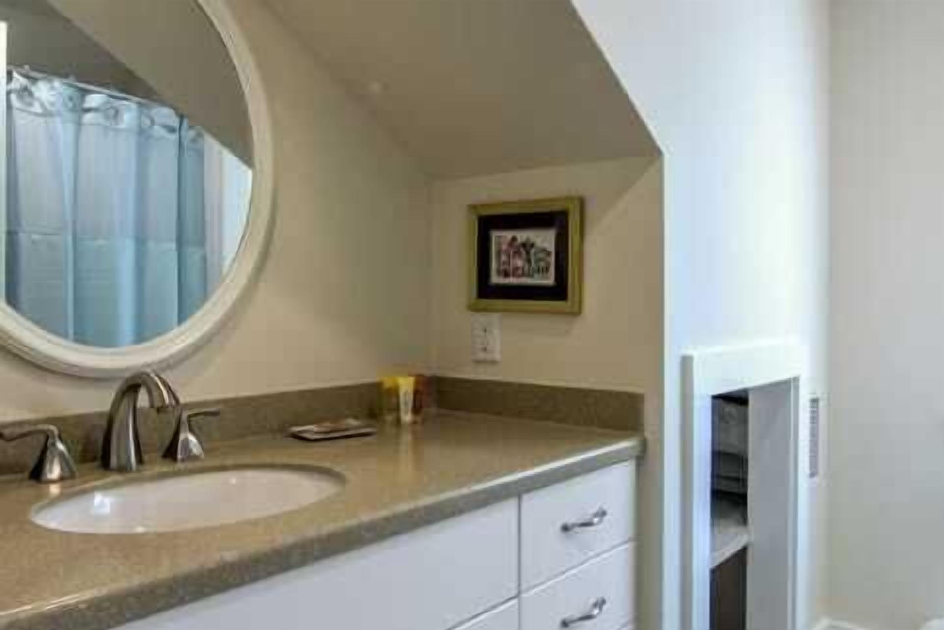 A bathroom with a round mirror, a sink, and a framed picture on the wall.