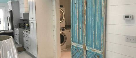 Une buanderie équipée d’un lave-linge et d’un sèche-linge, avec une porte bleue et un thermostat fixé au mur.