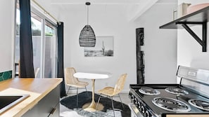A modern kitchen with a black stove, white dining table, and wicker chairs. - The Marley Hotel by AvantStay | 20 OCC Full Hotel Buyout in Palm Springs w/ Pool & Hot Tub! (Palm Springs)