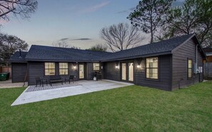 Una casa moderna con porche cubierto, césped y fachada oscura.
