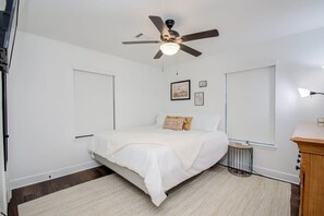 Un dormitorio con cama, ventilador de techo, mesita de noche y una alfombra pequeña.