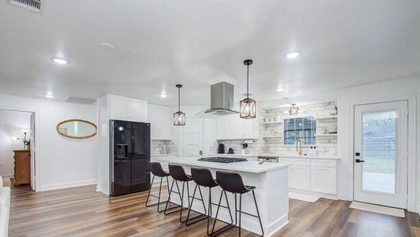 A modern kitchen with a central island, bar stools, and pendant lighting.