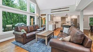 A spacious living area with leather sofas, a wooden coffee table, and large windows offering a view of the outdoors.