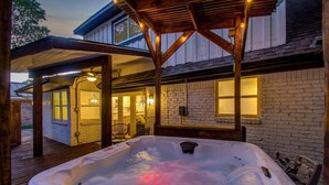 Een hottub onder een houten pergola, met een bakstenen muur en ramen op de achtergrond.