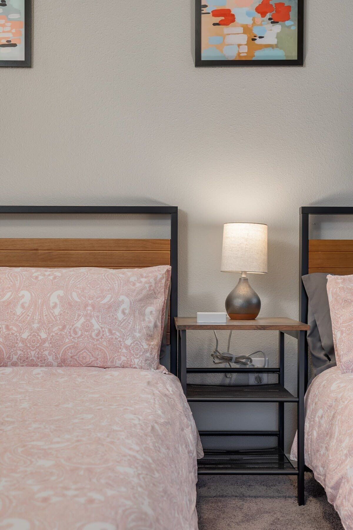 Une chambre d’hôtel avec deux lits, une table de chevet avec une lampe et des œuvres d’art accrochées aux murs.