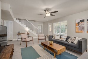 A living room with a sofa, coffee table, chairs, a TV, and a staircase. - Heart of Dallas - Mansion with Backyard Pool Oasis (Dallas)