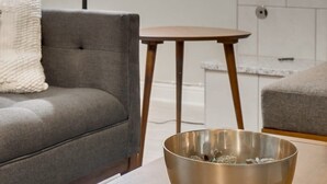 Moderni olohuone, jossa on harmaa sohva, pieni puinen pöytä ja metallinen kulho pöydällä.