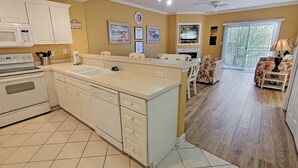 A kitchen with white cabinets, a microwave, and a stove. There is a dining area with a table and chairs. The walls are decorated with framed pictures.
