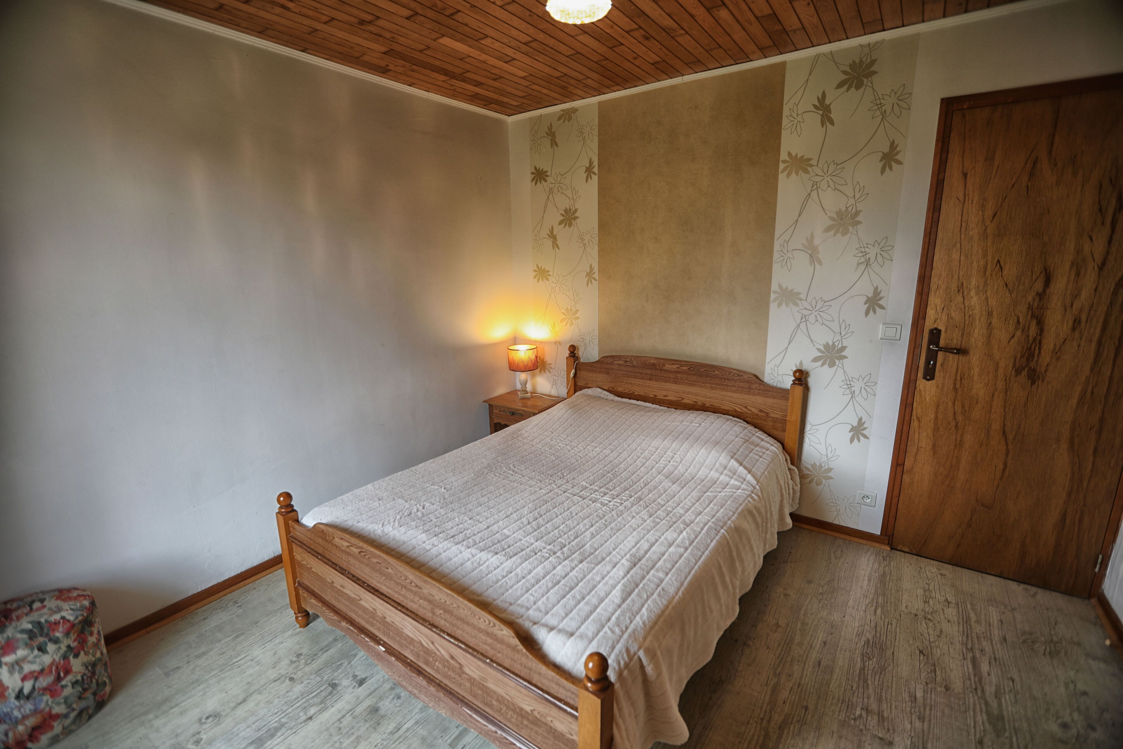 A bedroom with a wooden bed, a nightstand with a lamp, and a door.