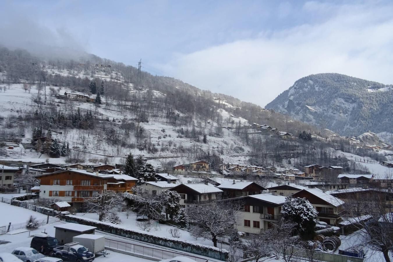 Un village enneigé, avec ses maisons traditionnelles en bois, un paysage montagneux en toile de fond et un ciel dégagé.