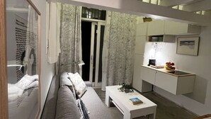 Ett modernt vardagsrum med en grå soffa, ett vitt soffbord och ett litet vitt skrivbord med en lampa.