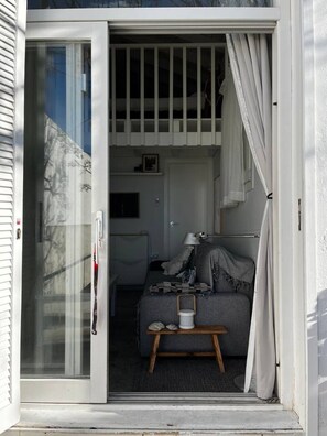 Et værelse med skydedør, en seng med tæppe, et lille bord med lampe og et vindue med gardiner.