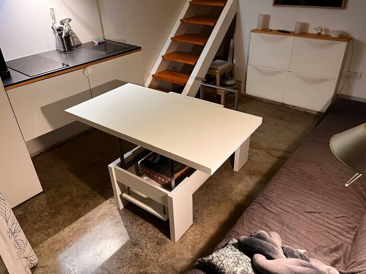 A compact living space with a kitchenette, a foldable table, a sofa, and a staircase.