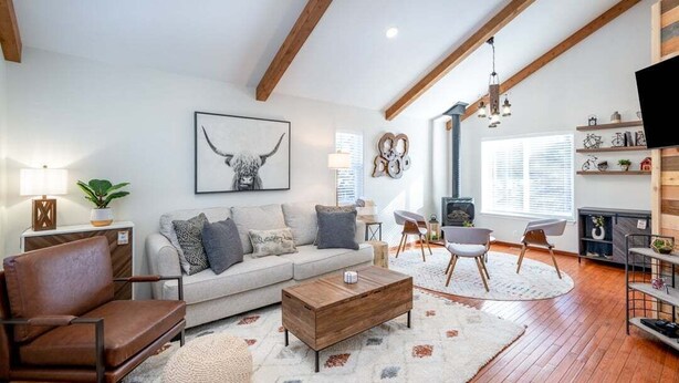 A spacious living room with a wooden coffee table, a sofa, and a TV mounted on the wall. - Bluebird Day - Mountain Escape, Cozy a 3-bedroom home in Bend, OR. (Bend)