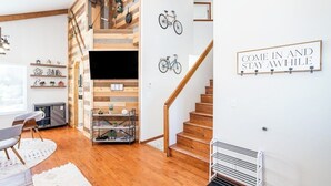 A modern living room with a wooden staircase, a mounted TV, and a 'Come in and stay awhile' sign. - Bluebird Day - Mountain Escape, Cozy a 3-bedroom home in Bend, OR. (Bend)