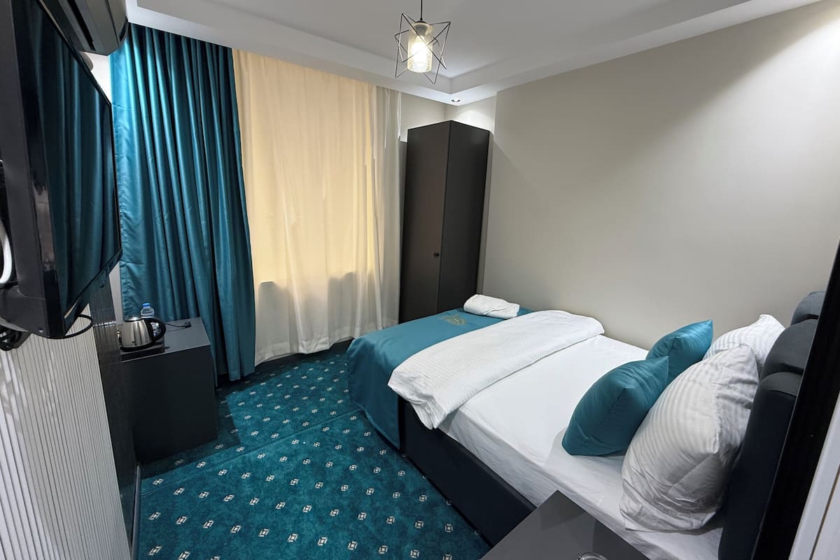 Habitació d'hotel amb llit, escriptori, armari i finestra amb cortines.