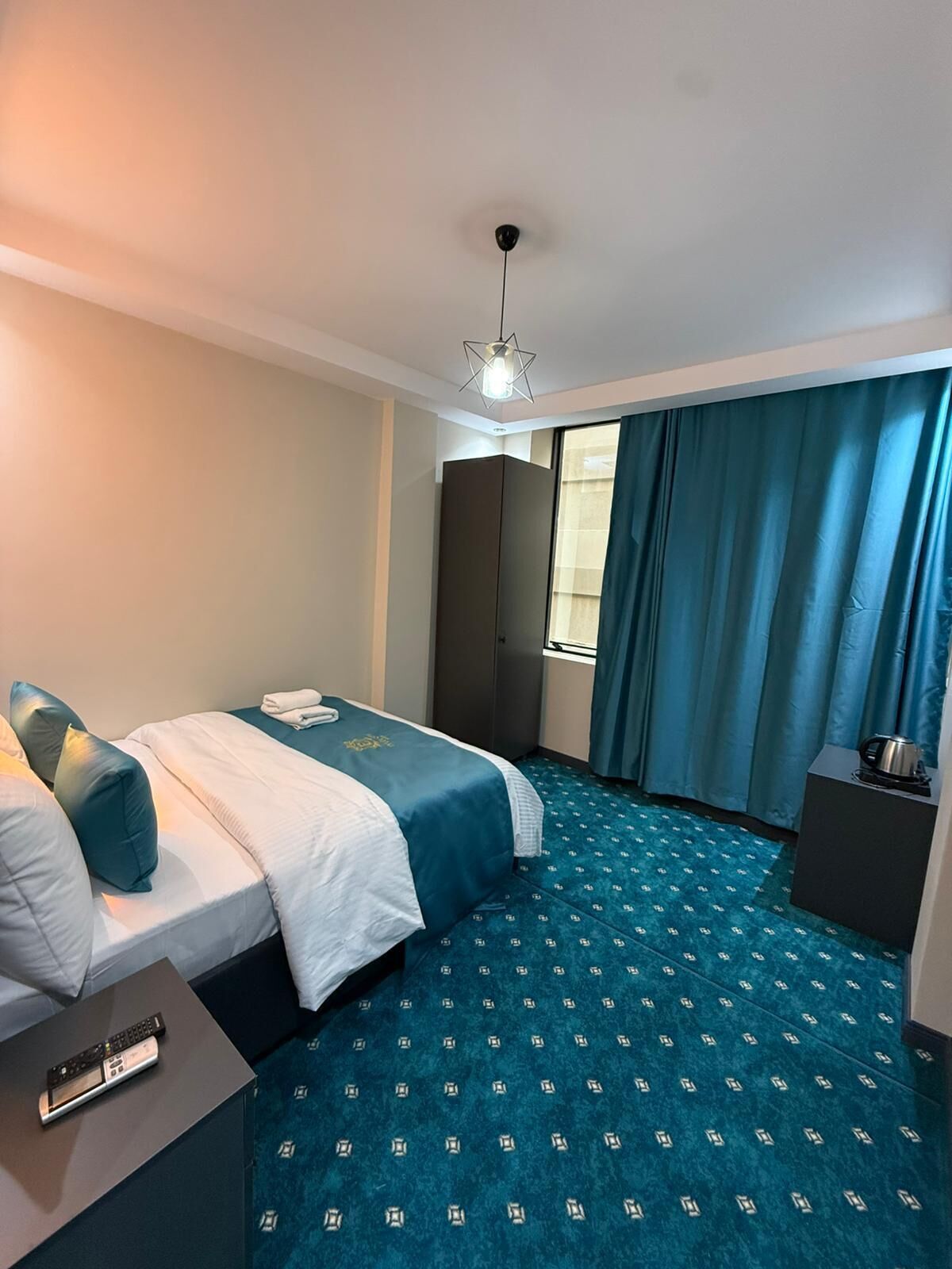 A hotel room with two beds, a wardrobe, a desk with a kettle, and a patterned carpet.
