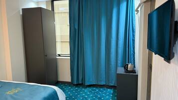 A hotel room with a bed, a wardrobe, a small table with a kettle, and a television.