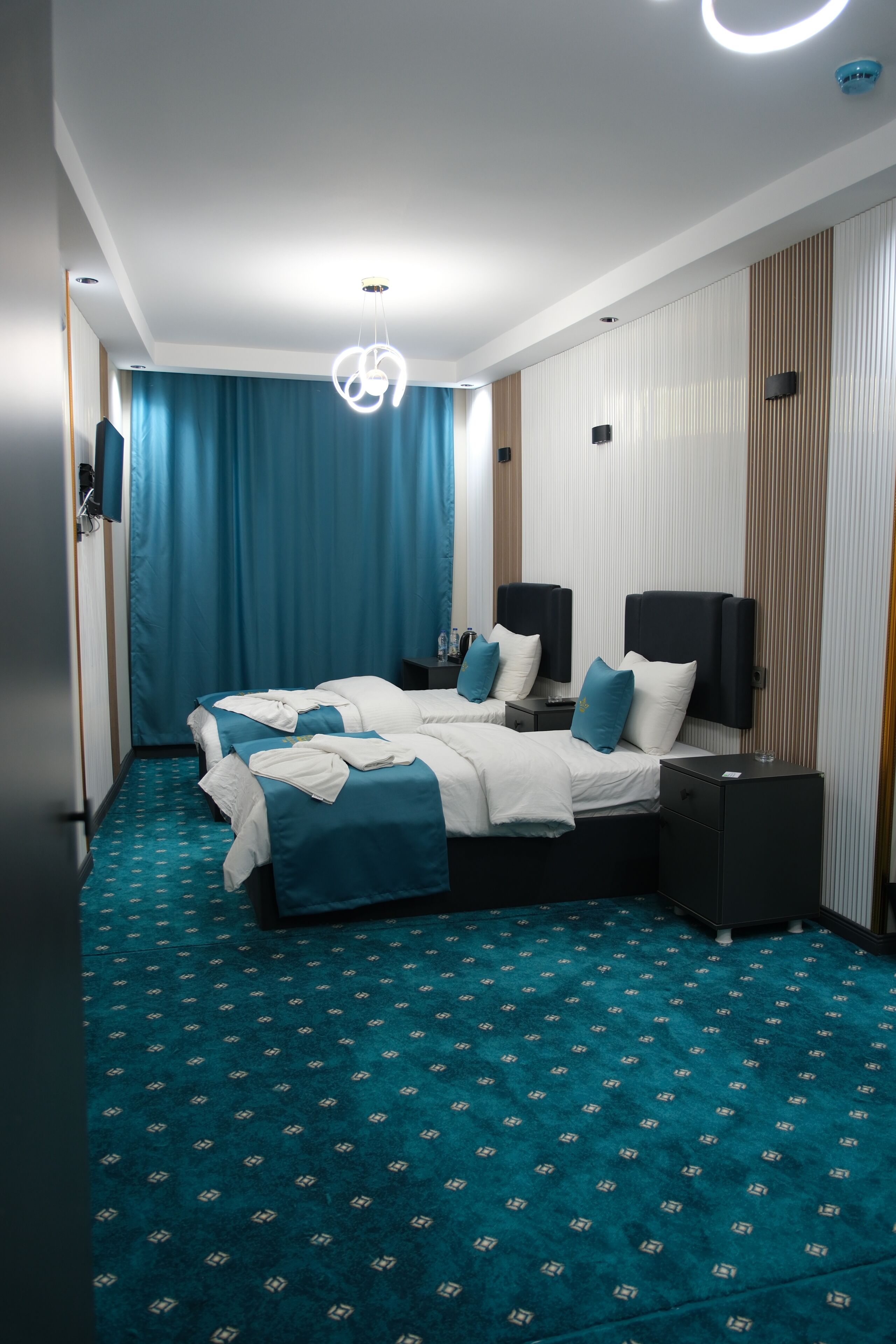 A hotel room with two beds, a blue carpet, and a modern ceiling light fixture.