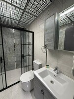 Egy modern fürőszoba, amelyben WC, mosdókagyló és zuhanyzó található.