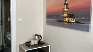 Habitación de hotel con kitchenette pequeña, un cubo de basura y un cuadro de una torre en la pared.