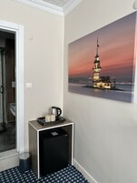 Egy szállodai szoba, amelyben van egy kis konyhasarok, egy szemeteskosár, és a falon egy torony képét ábrázoló festmény található.