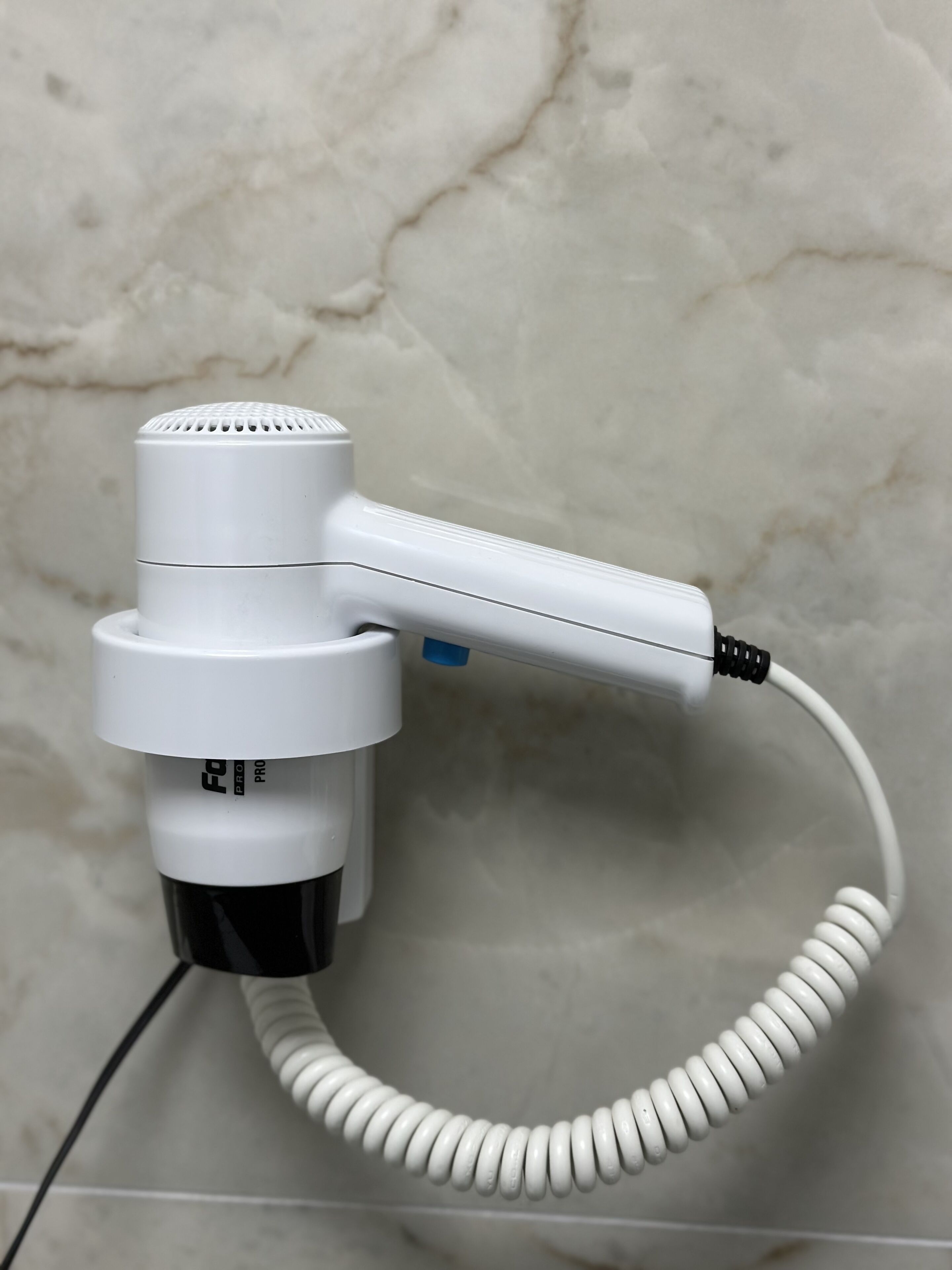 A white hair dryer with a coiled cord, connected to a power source.