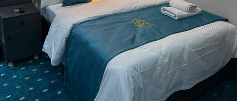 Una cama bien hecha con una colcha azul y blanca, un cabecero y una mesita de noche con una lámpara.