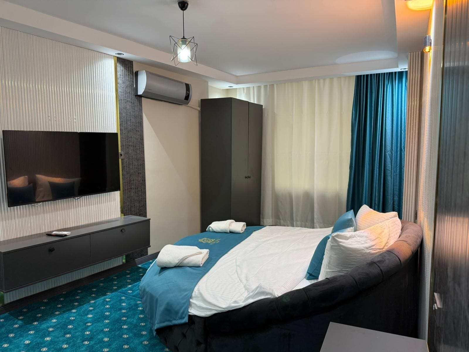 A hotel room with a bed, a TV, a wardrobe, and an air conditioning unit.