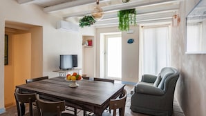 A dining area with a wooden table, chairs, a television, and a fruit bowl.