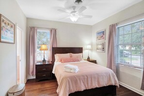 A bedroom with a bed, nightstands, a ceiling fan, and a window with curtains.