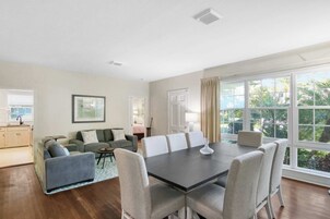 Amplia sala de estar con una gran mesa de comedor, asientos cómodos, una zona de cocina y ventanas grandes con vistas a zonas verdes.