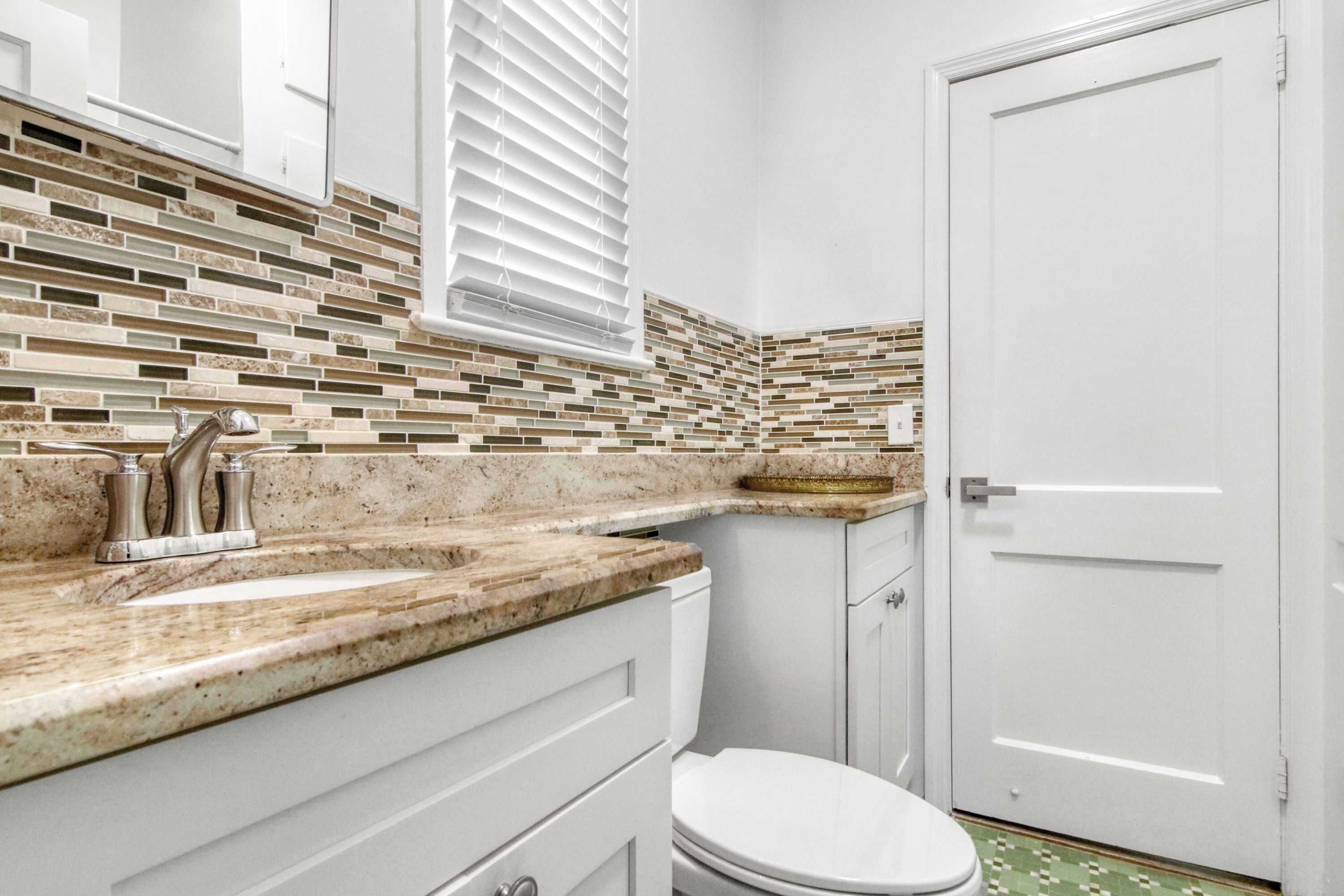 A bathroom with a tiled backsplash, a sink with a faucet, a toilet, and a door.
