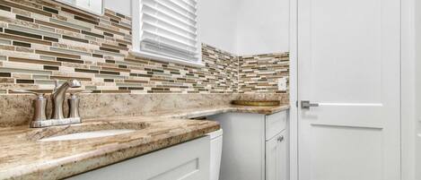 A bathroom with a tiled backsplash, a sink with a faucet, a toilet, and a door.