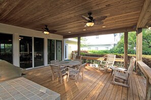 A wooden deck with a table and chairs, a ceiling fan, and a view of a house and greenery.