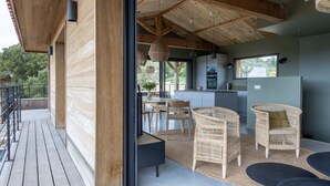 Una cocina moderna con un ventanal grande, un comedor con mobiliario de mimbre y una terraza de madera.