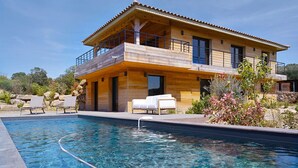 Una casa moderna de madera con piscina, mobiliario exterior y un muro de piedra.