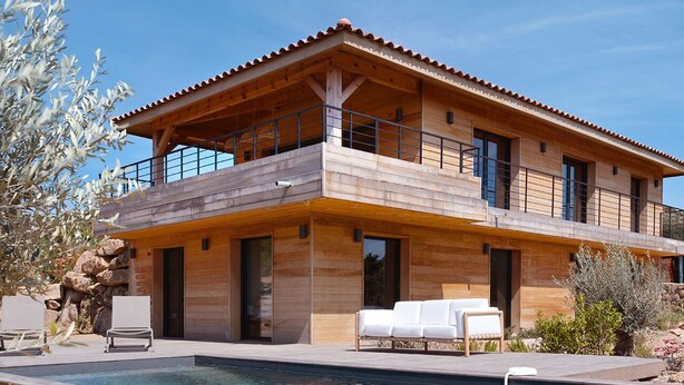Una casa moderna de dos pisos con fachada de madera, un balcón y una piscina.