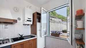 Une cuisine équipée d’une cuisinière à gaz, d’un évier, de meubles blancs et d’une fenêtre donnant sur un balcon.