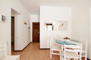 Un coin repas avec une table ronde, des chaises blanches, un saladier de fruits et un miroir au mur.